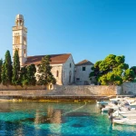 Türkisfarbenes Wasser der Adria-Bucht auf der Insel Hvar mit Franziskanerkloster und Booten in der Region Dalmatien, Kroatien bei Sonnenaufgang